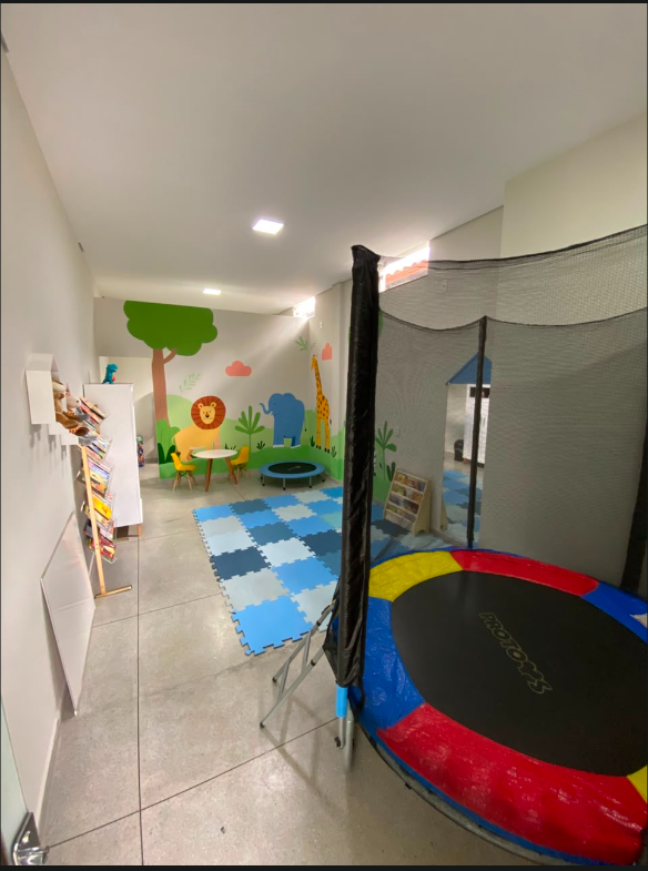 Visão ampla do espaço infantil com cama elástica, tatame, brinquedos e mural de animais